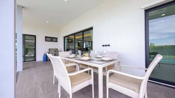 Uma área de refeições com mesa de vidro, cadeiras de vime e uma churrasqueira.