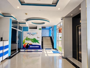 A modern lobby with a reception desk, a staircase, and a large welcome sign.