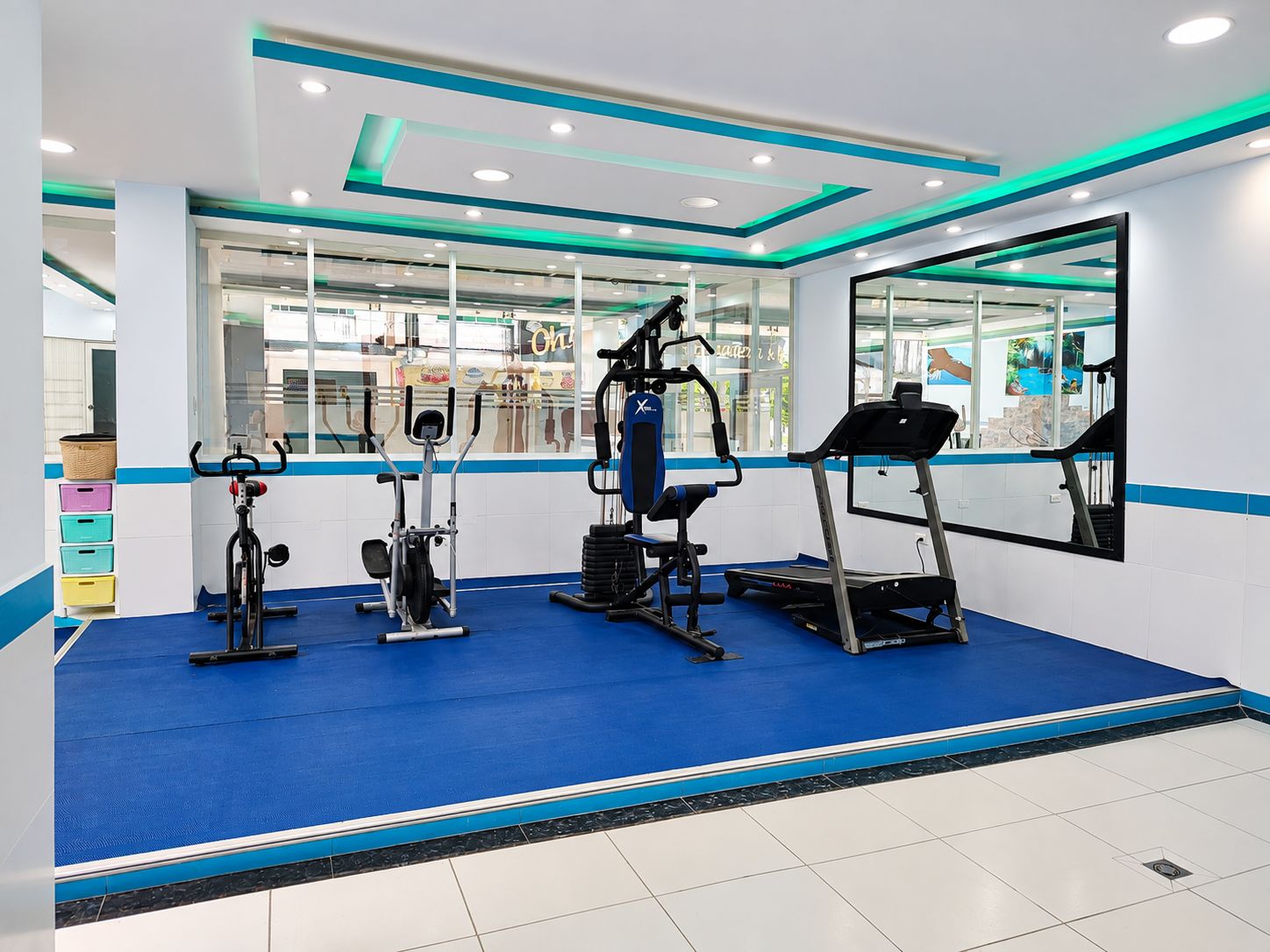 Ein Fitnessraum mit Trainingsgeräten, blauem Boden und einem großen Spiegel.