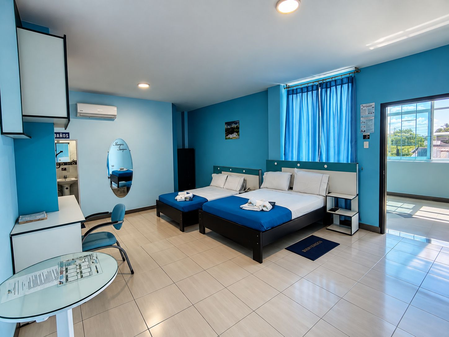 Camera d'albergo con due letti, una scrivania, una sedia, un bagno e vista sull'esterno.