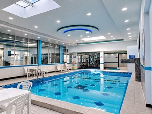An indoor swimming pool with clear blue water, surrounded by white chairs and a tiled floor. - Hotel Marques Amazonico (Nueva Loja)