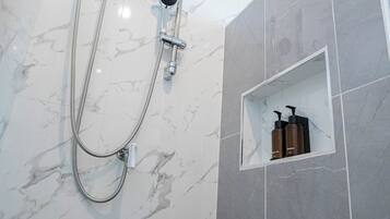 Un baño con ducha, inodoro y repisa con artículos de aseo.