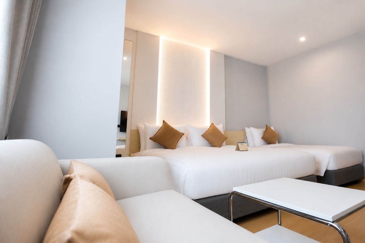 A hotel room with two beds, a sofa, and a small table.