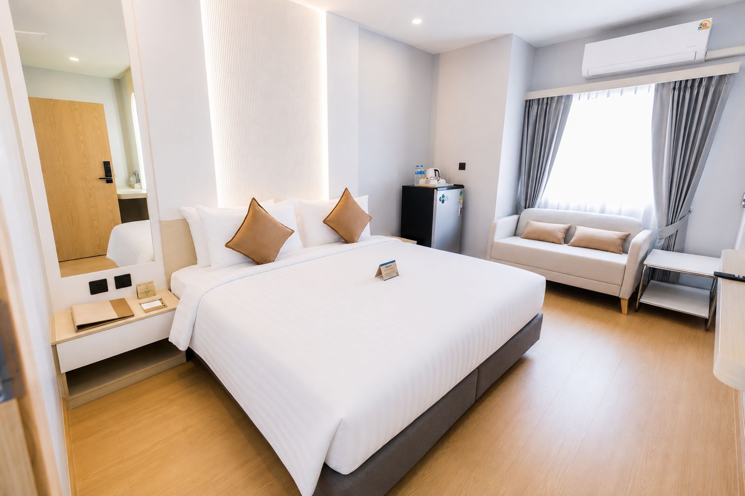 Una habitación de hotel moderna con una cama grande, un sofá, un escritorio y un equipo de aire acondicionado.