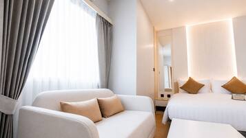 Una habitación de hotel con sofá, cama, mesita de noche y espejo.