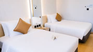 A hotel room with two beds, each with white bedding and a single brown pillow. There is a bedside table with a lamp and a small card.
