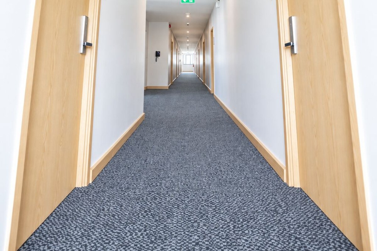 Un pasillo de hotel con pisos alfombrados, puertas de madera y una lámpara en el techo.