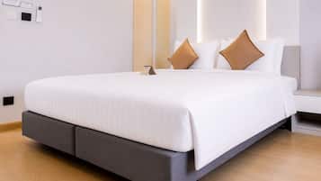 A modern hotel room with a large bed, grey upholstered headboard, white bedding, and a bedside table with a lamp.