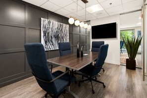 A conference room with a dark wood table, four blue chairs, a large abstract painting, a flat-screen TV, and a potted plant. - Blueground | Fulton River District, gym, nr Park (Chicago)