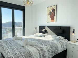 A bedroom with a large bed, a nightstand, a wall-mounted light, and a painting. - Penthouse in Nerja With Sea Views & Pool (Nerja)