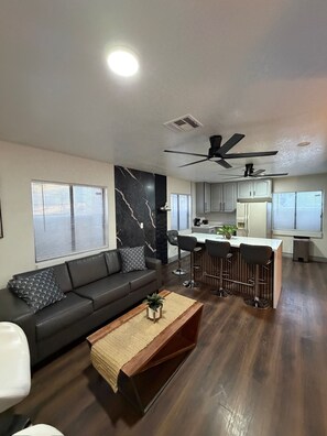 A modern living room with a dark wood floor, a grey sofa, and a coffee table with a plant. - Luxury 8BR HOME + Private Basement Apartment, Pool, Jacuzzi, Sauna & Gym (Las Vegas)