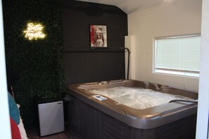 Ein Whirlpool mit Bedienfeld, ein kleiner Kühlschrank, ein Neon-Schild und ein Poster an der Wand.