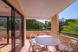 Een balkon met een tafel, stoelen, een schuifpui en uitzicht op groen.
