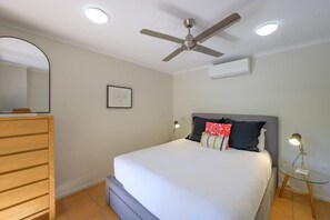 Ein Schlafzimmer mit einem Bett, einem Deckenventilator, einem Nachttisch mit Lampe und einer Kommode.