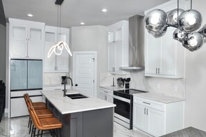A modern kitchen with white cabinetry, a central island, stainless steel appliances, and a pendant light. - Spacious New 4-bedroom light-house in perfect Dallas with Resort style living. (Dallas)