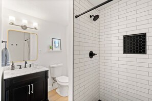 A bathroom with a white tiled shower, a sink with a mirror, and a toilet. - The Desert Peach | Near ASU, Old Town + Sky Harbor (Tempe)