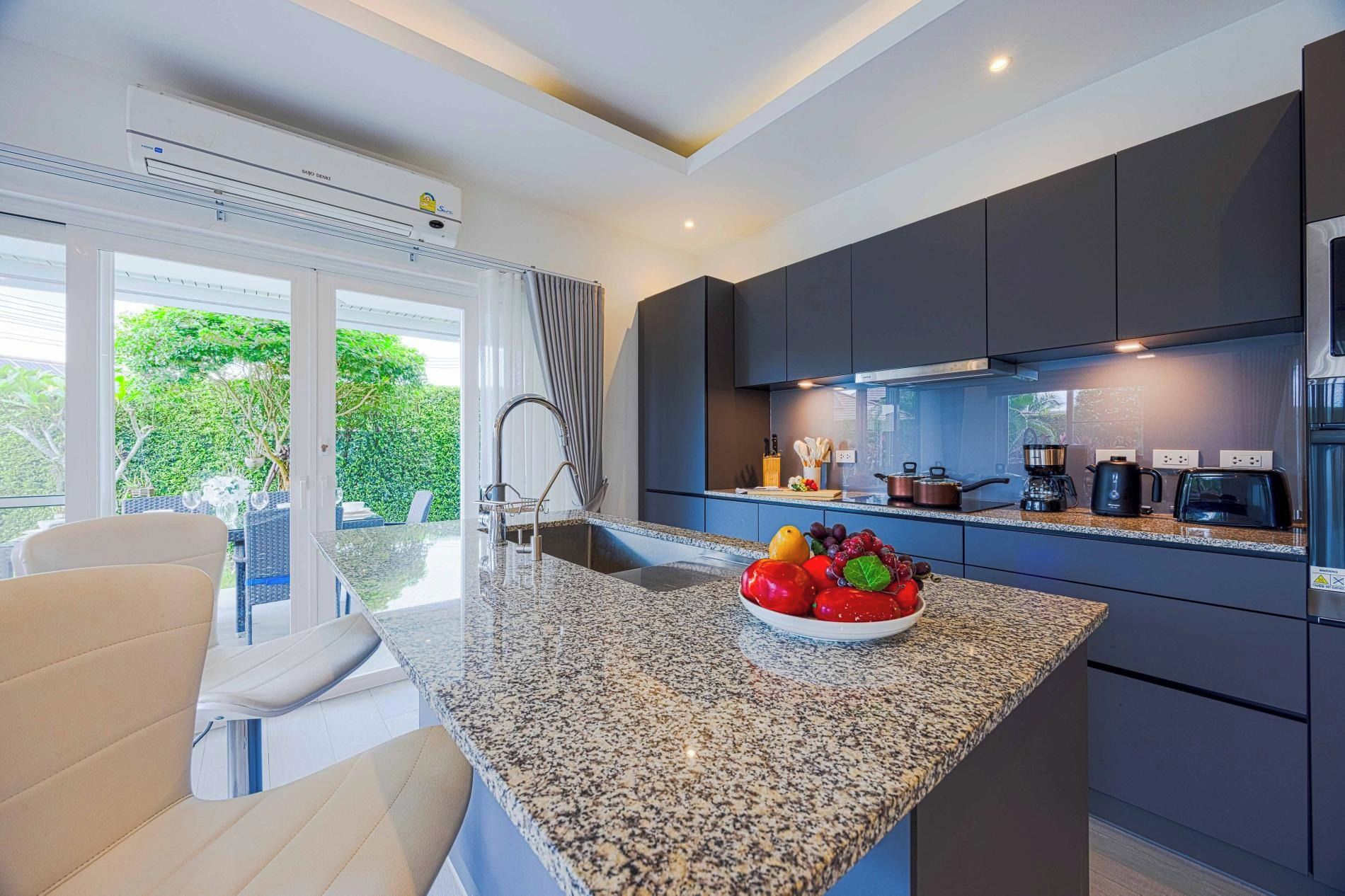 A modern kitchen with a granite countertop, dark cabinetry, and a bowl of fruit.