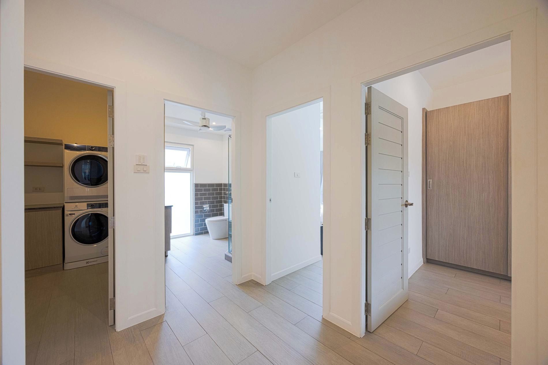 A hallway with a laundry area, a bathroom, and a wooden door.