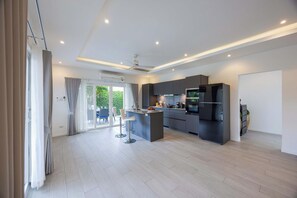 A modern kitchen with a central island, built-in appliances, and a sliding glass door leading to a patio. - New Private Luxury Pool Villa (ML132) (Hua Hin)