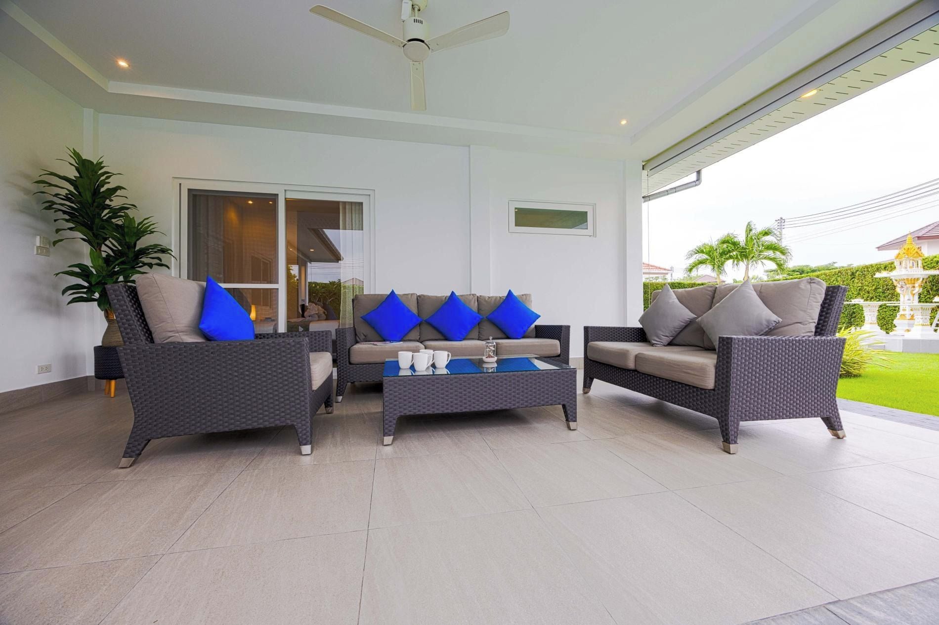Una sala moderna con mobiliario de mimbre, un ventilador de techo y vistas a un jardín.