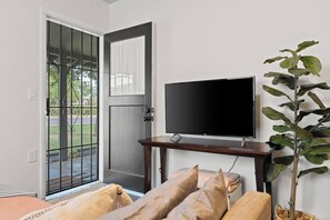 A room with a TV on a stand, a door with a view to the outside, and a potted plant. - Arcadia Studio | Private Entry, Desk + Fast WiFi (Phoenix)