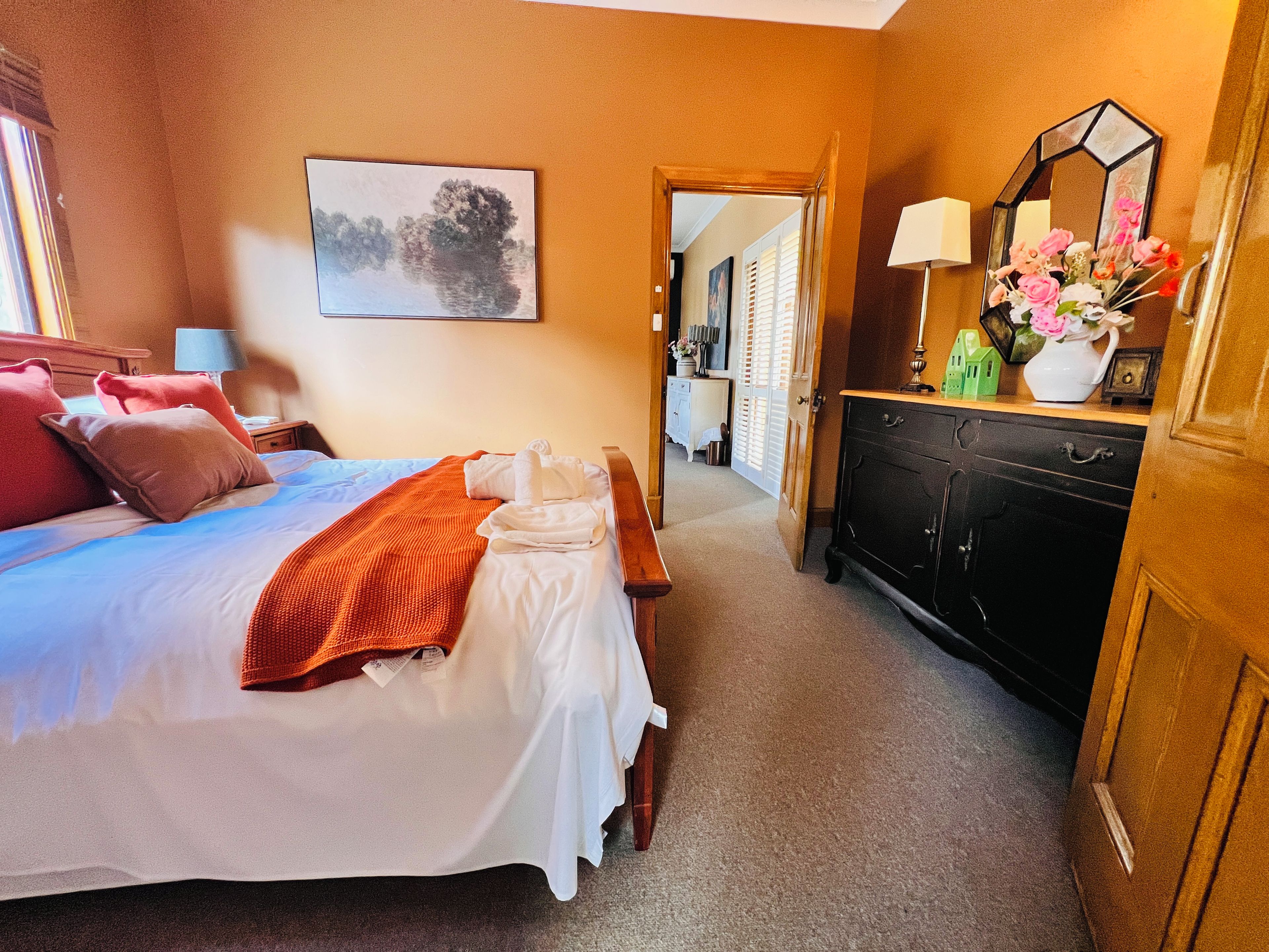 A hotel room with a bed, bedside table, dresser, and a painting on the wall.