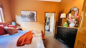 Una habitación de hotel con cama, mesita de noche, cómoda y un cuadro en la pared.