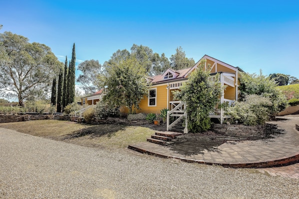 A yellow house with a balcony, surrounded by trees and a gravel driveway. - Vineyard Charm House | McLaren Vale Retreat (Blewitt Springs)