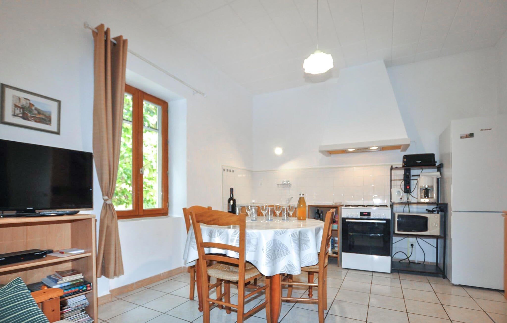 A compact living space with a dining table, chairs, a television, kitchen appliances, and a window with curtains.