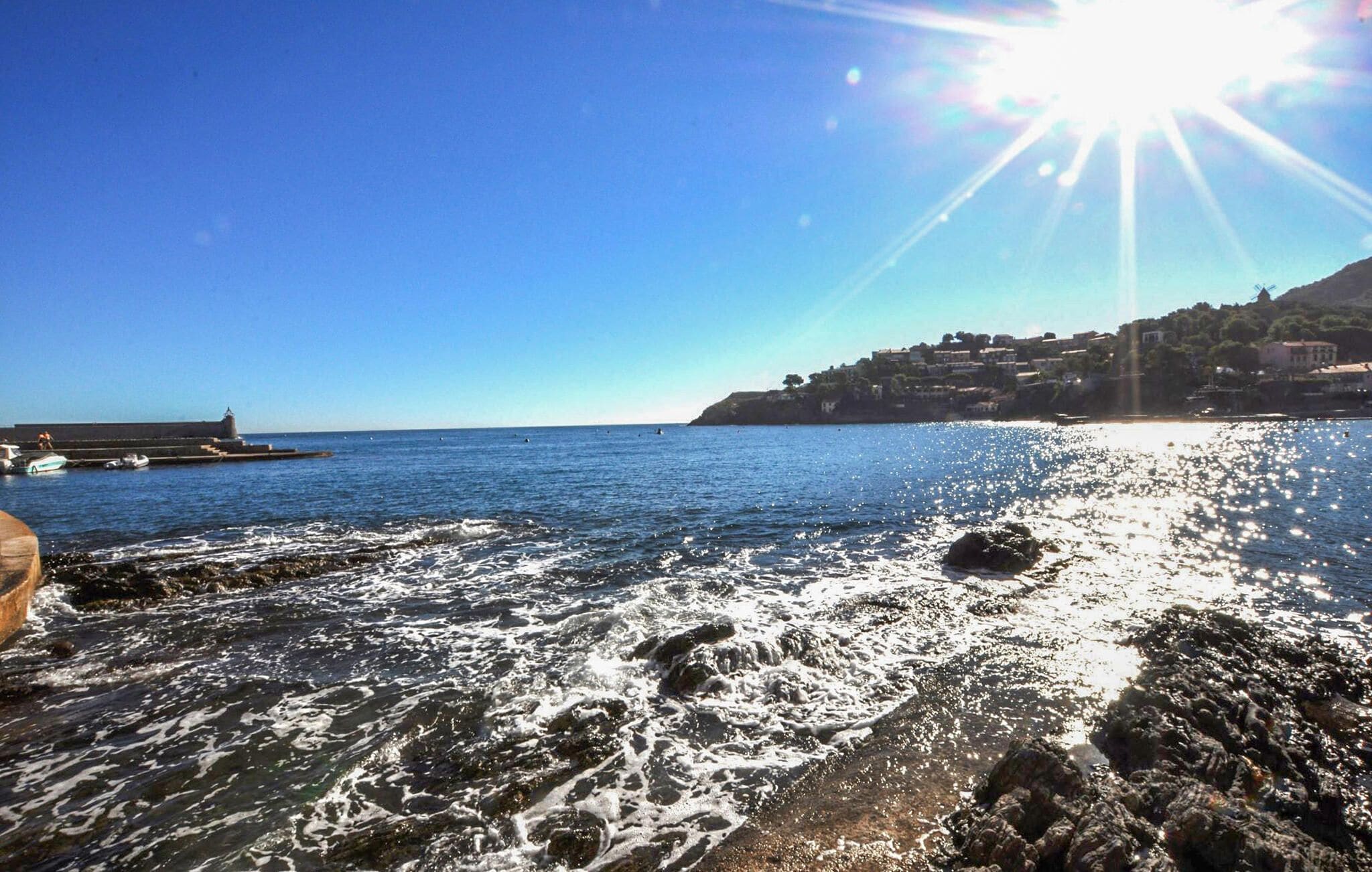 A coastal scene with rocky shoreline, clear blue sky, and distant buildings.