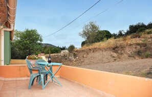 Eine Terrasse im Freien mit Tisch und Stühlen, einer Weinflasche und Blick auf einen Hügel.