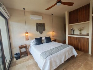 A bedroom with a bed, ceiling fan, wall-mounted air conditioner, macrame wall hanging, and a small bedside table with a lamp. - Luxury 2BR Penthouse in the Jungle. Nature, Pools & Cenotes in Tulum (Tulum)