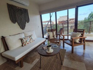 Ein modernes Wohnzimmer mit einer Couch, Sesseln, einem Couchtisch und einem großen Fenster mit Blick ins Freie.