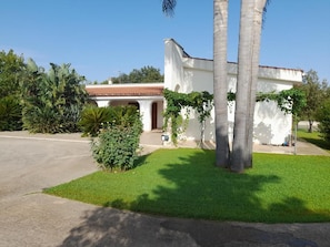 A white building with a red-tiled roof, surrounded by greenery and palm trees. - Babette's House (Puglia)