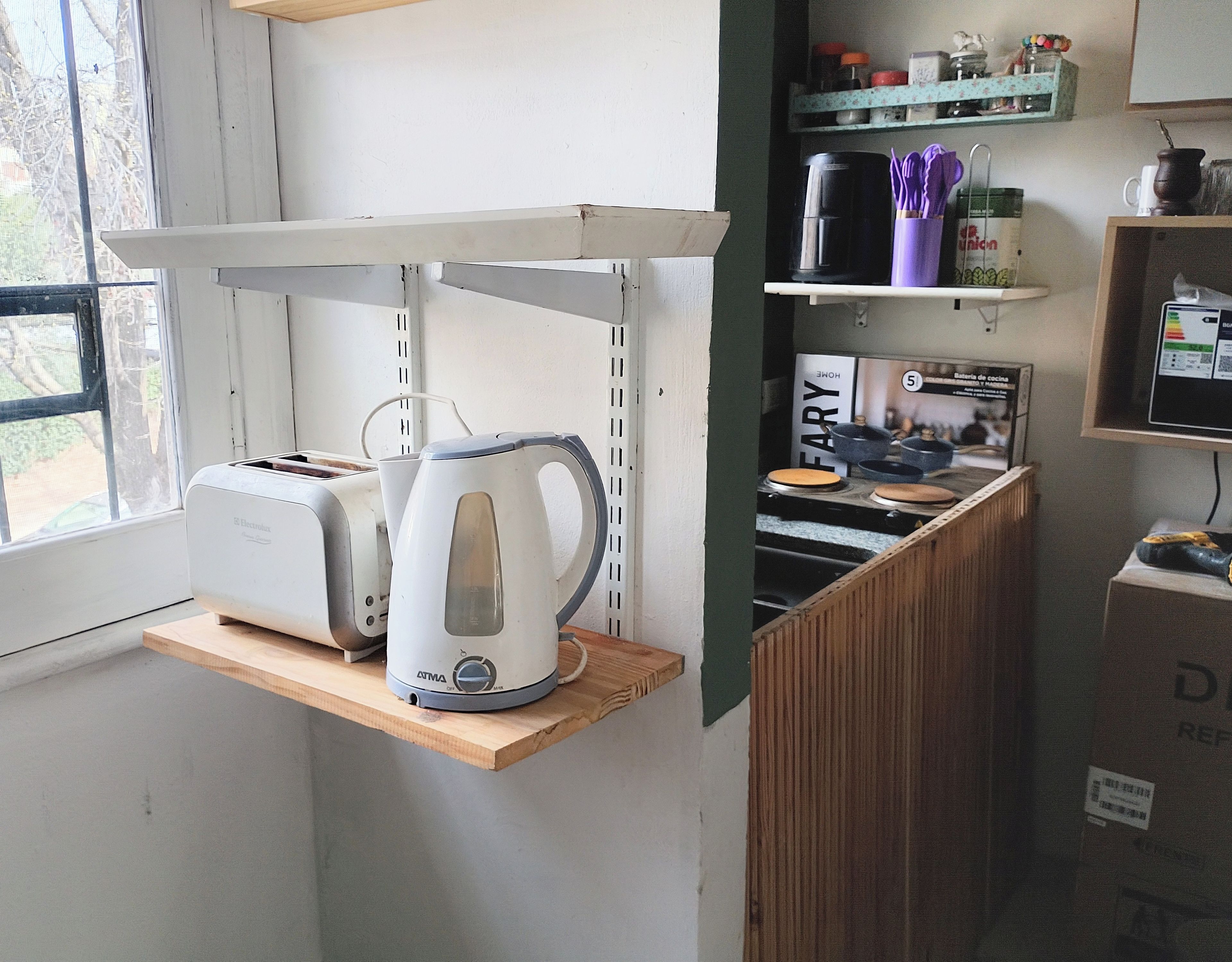 A kitchen with a toaster, kettle, and a shelf with kitchenware.
