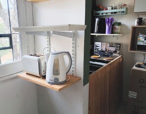 A kitchen with a toaster, kettle, and a shelf with kitchenware.