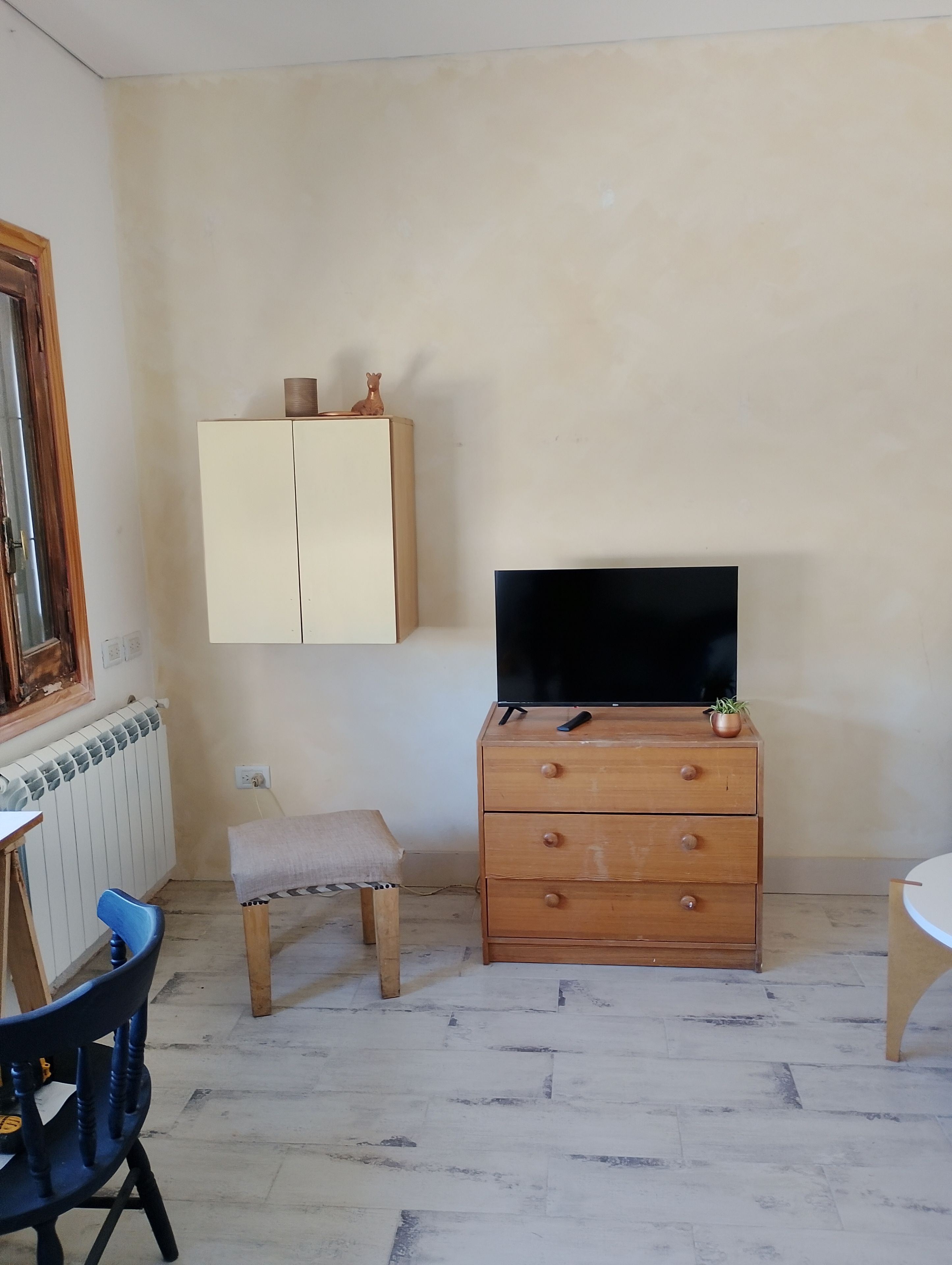 A small room with a wooden cabinet, a television on top, a small stool, and a blue chair.