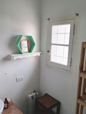 Een badkamer met een witte wastafel, een klein houten krukje, een groene plank met een lijst eromheen, en een raam met een witte rand.