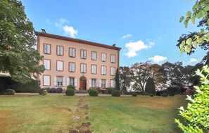Ein großes, mehrstöckiges Gebäude mit einer symmetrischen Fassade, einem zentralen Eingang und einem gepflegten Rasen davor.