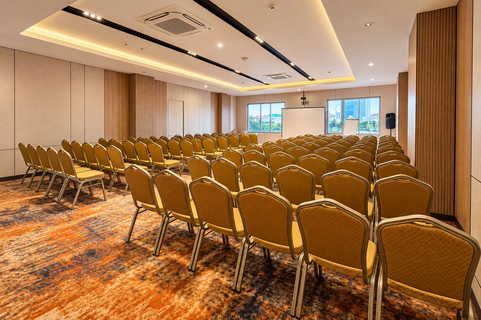 Une salle de conférence avec des rangées de chaises, un sol recouvert de moquette et une grande fenêtre donnant sur un paysage.