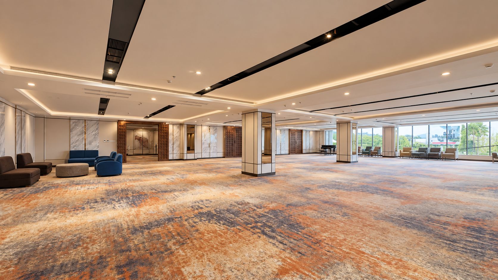 Un'ampia hall d'albergo con tappeto decorato, zone relax e ampie finestre che offrono vista sull'esterno.
