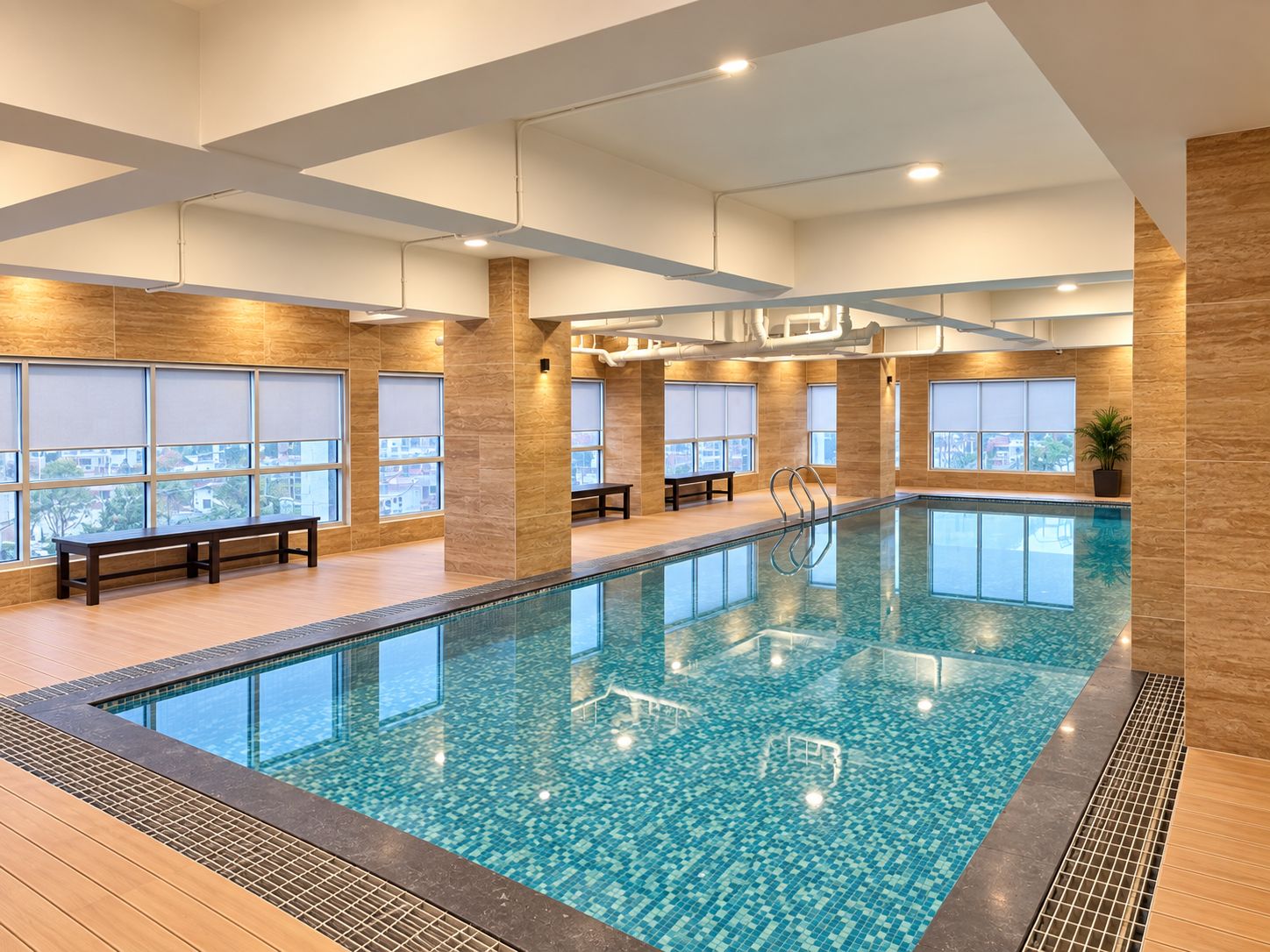 Ein Hallenbad mit Fliesenboden, Sitzbänken und großen Fenstern.