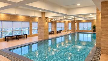 Ein Hallenbad mit Fliesenboden, Sitzbänken und großen Fenstern.