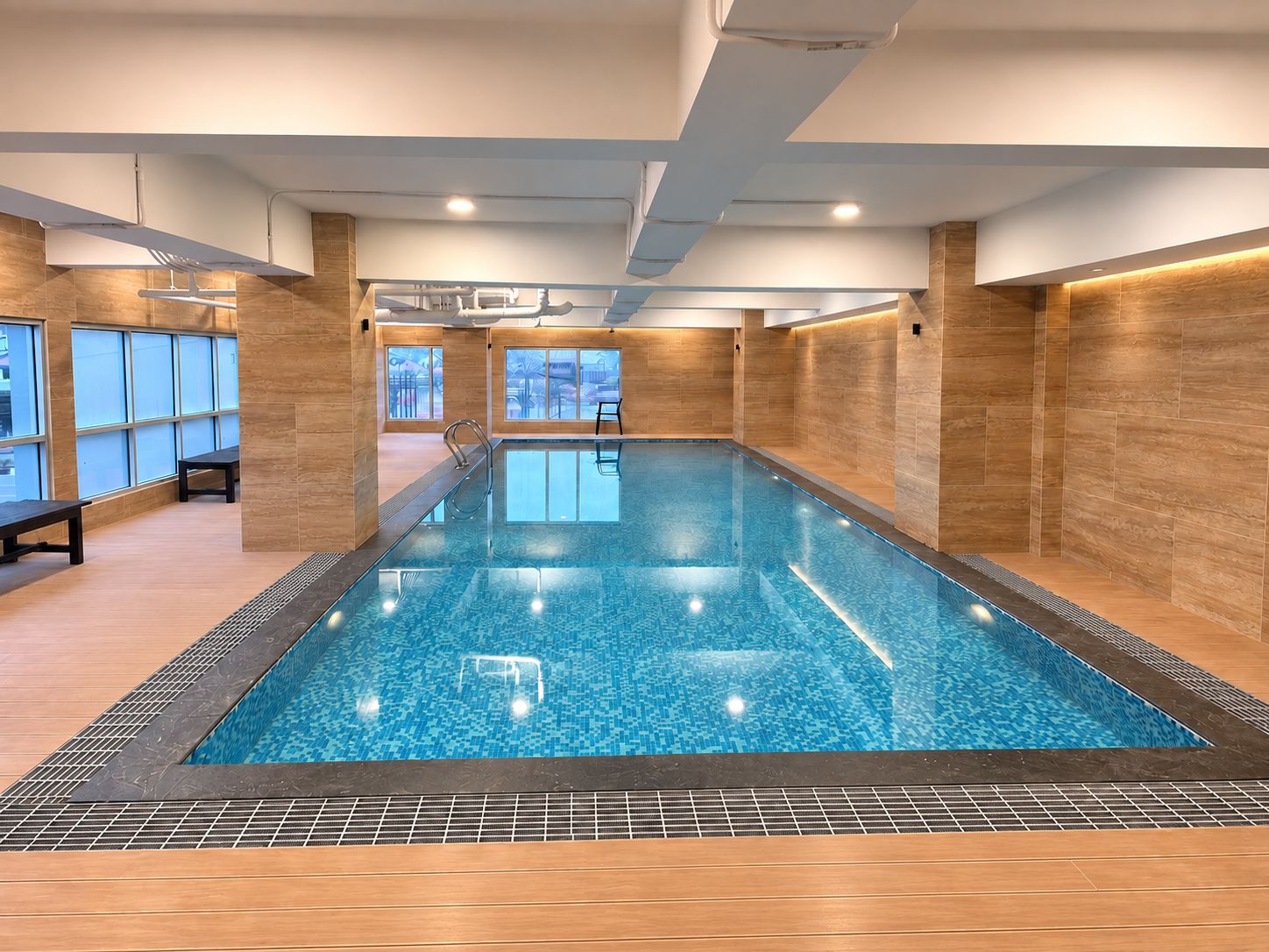 An indoor swimming pool with clear blue water, surrounded by wooden walls and benches.