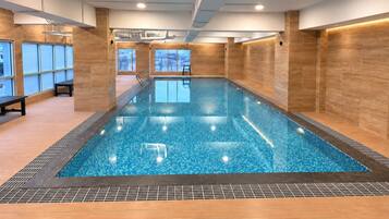 An indoor swimming pool with clear blue water, surrounded by wooden walls and benches.