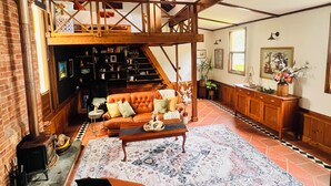 Un salon spacieux avec un haut plafond, une cheminée, un canapé, une table basse et une bibliothèque.