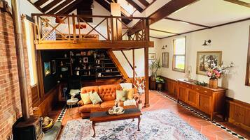 A spacious living room with a high ceiling, a fireplace, a sofa, a coffee table, and a bookshelf.