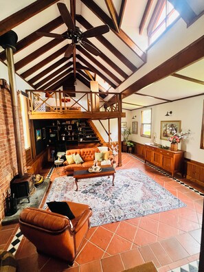 A spacious living room with a high ceiling, a fireplace, a sofa, a coffee table, and a bookshelf. - 5-bedroom vineyard cottage for groups McLaren Vale (Blewitt Springs)