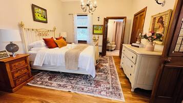 A bedroom with a bed, bedside tables, a dresser, a chandelier, and a rug.