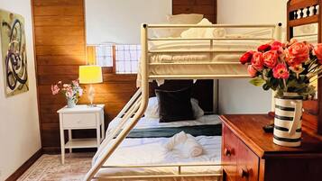 A bunk bed room with a wooden ceiling, a bedside table with a lamp, a dresser, and a rug.